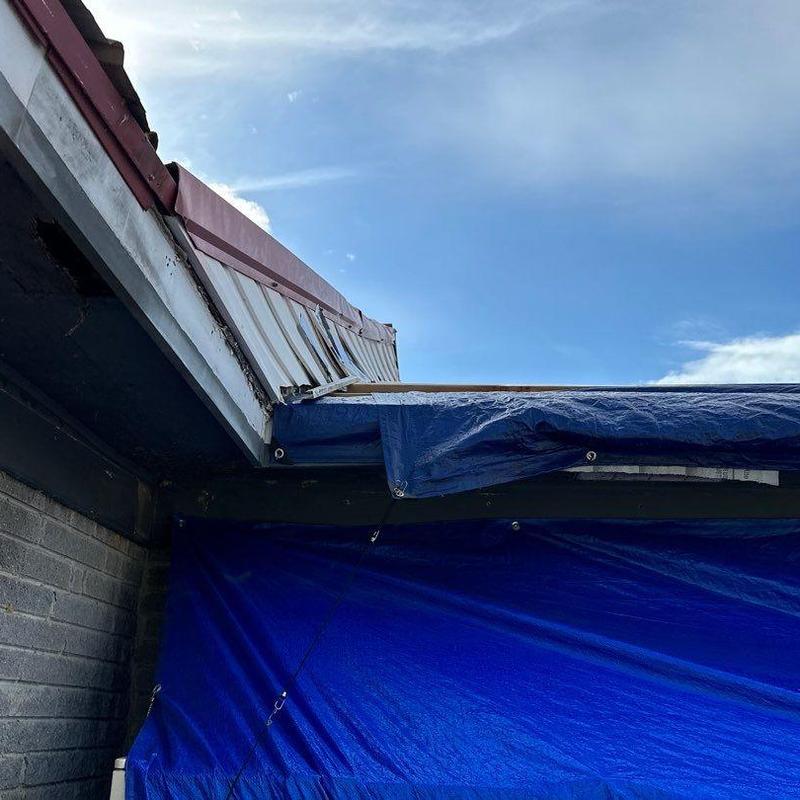 Metal roof edge with storm damage and protective tarp