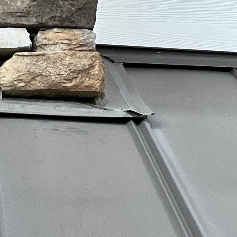 Metal roof panel with loose edge near stonework