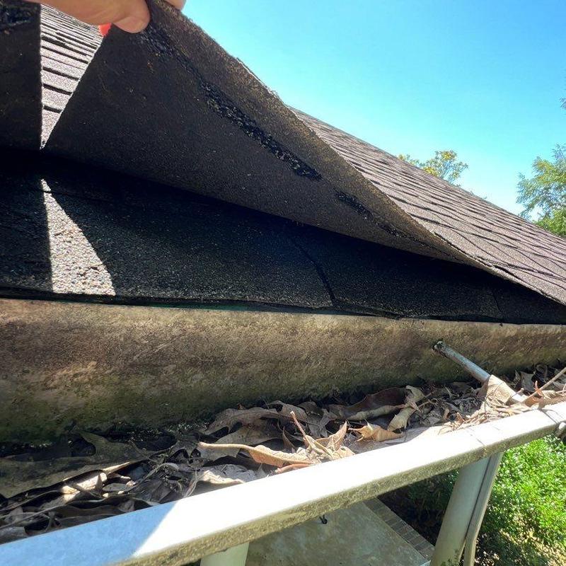 Roof shingles lifted to inspect hail damage and gutter debris