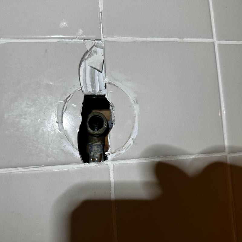 Drop ear plumbing fitting exposed in tiled wall hole