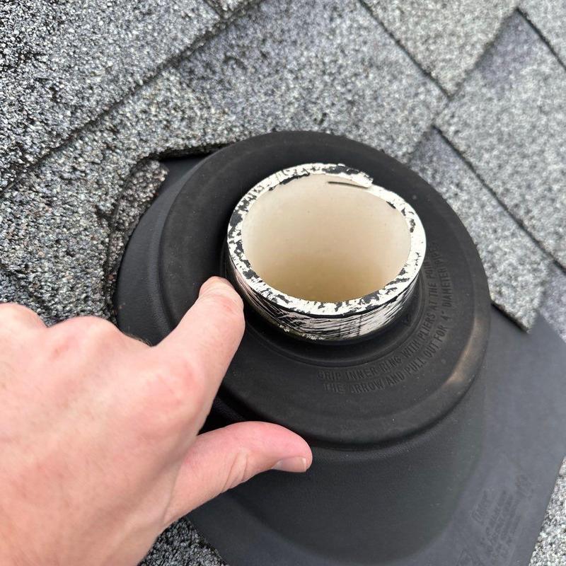 Roof pipe flashing on shingled roof with hand pointing