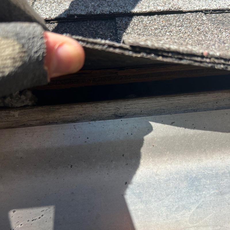 Roof shingles lifted to show underlying gap and damage