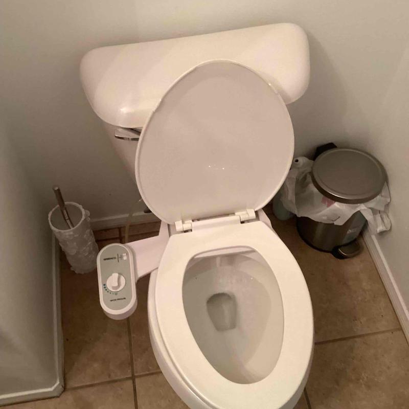 Toilet with bidet attachment in bathroom corner