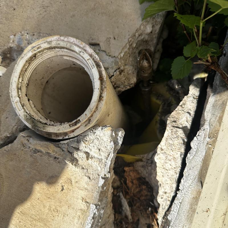 Broken outdoor cleanout pipe in cracked concrete ground