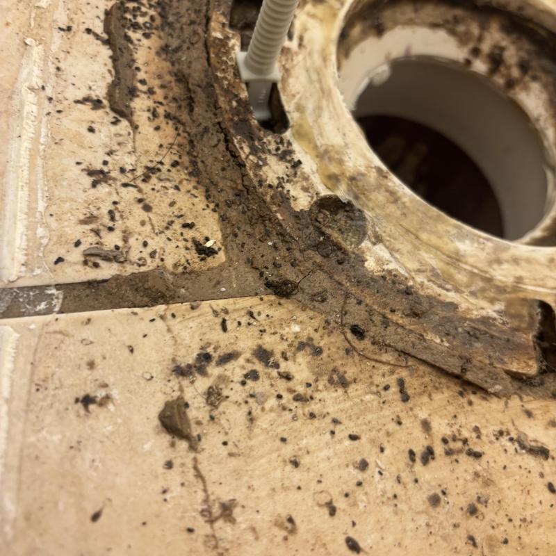 Toilet flange with dirt and corrosion buildup on tile floor