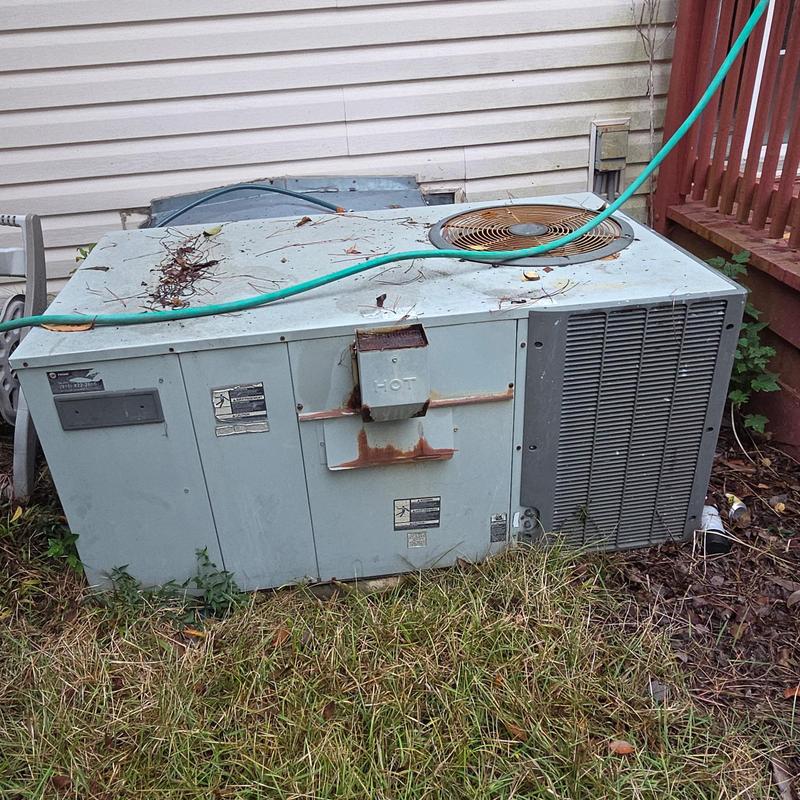 Rusted outdoor HVAC unit with debris and garden hose