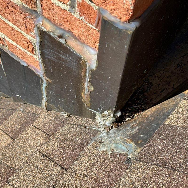 Roof flashing with sealant and shingle debris near brick wall