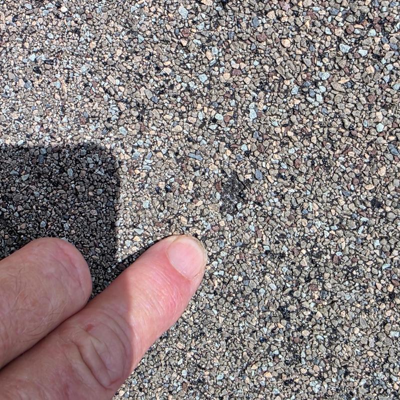 Roof shingle hail impact damage close-up with finger for scale