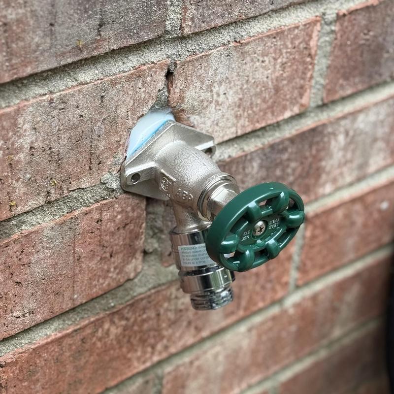 Hose bib with green handle installed on brick wall