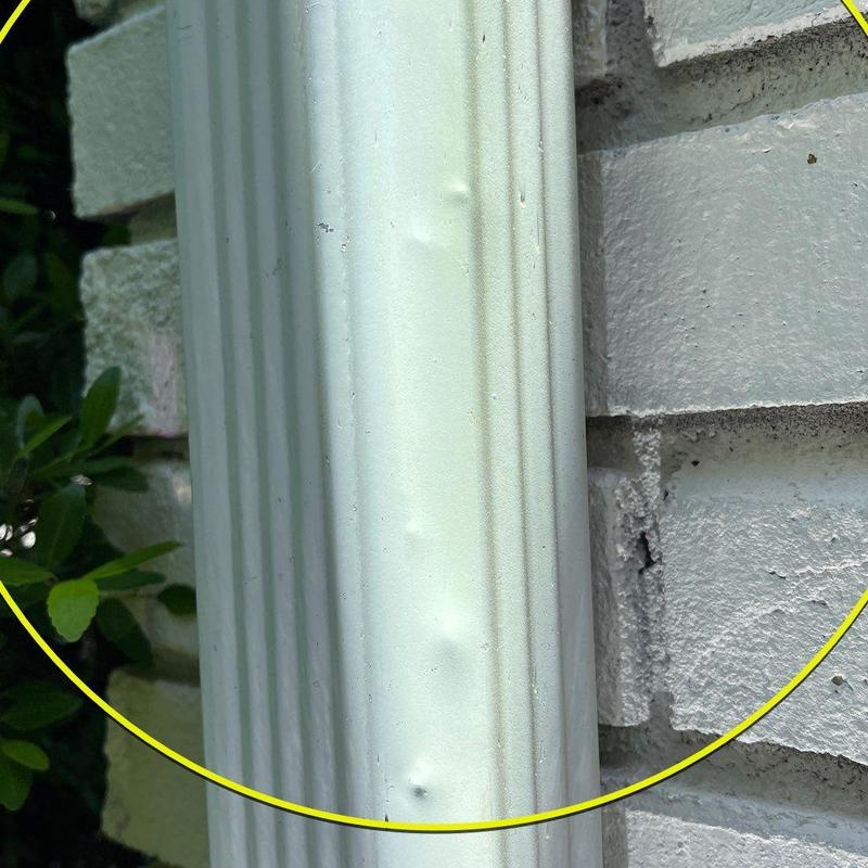 Downspout with dents on brick wall background