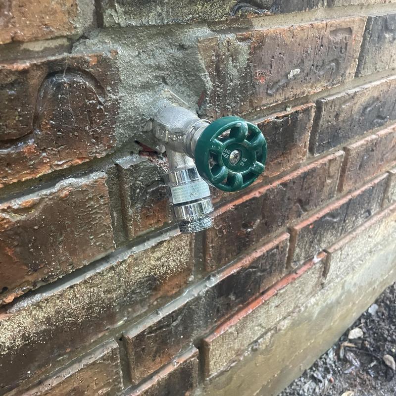 Outdoor hose bib with green handle on brick wall
