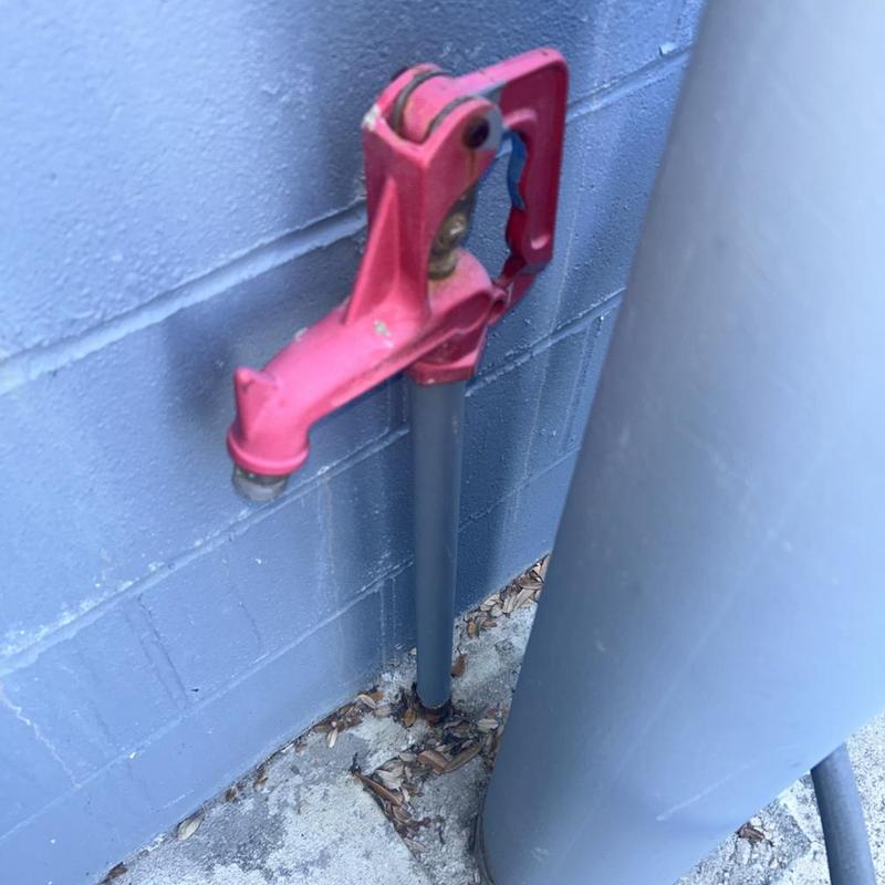 Outdoor water spigot with red handle on gray pipe