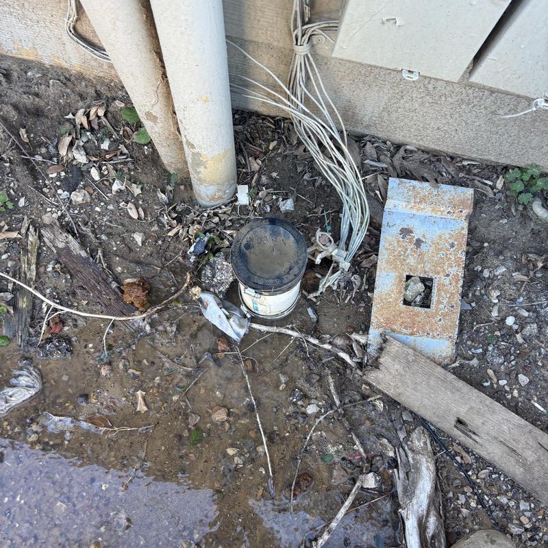 Sewer cleanout cap and exposed plumbing lines outdoors