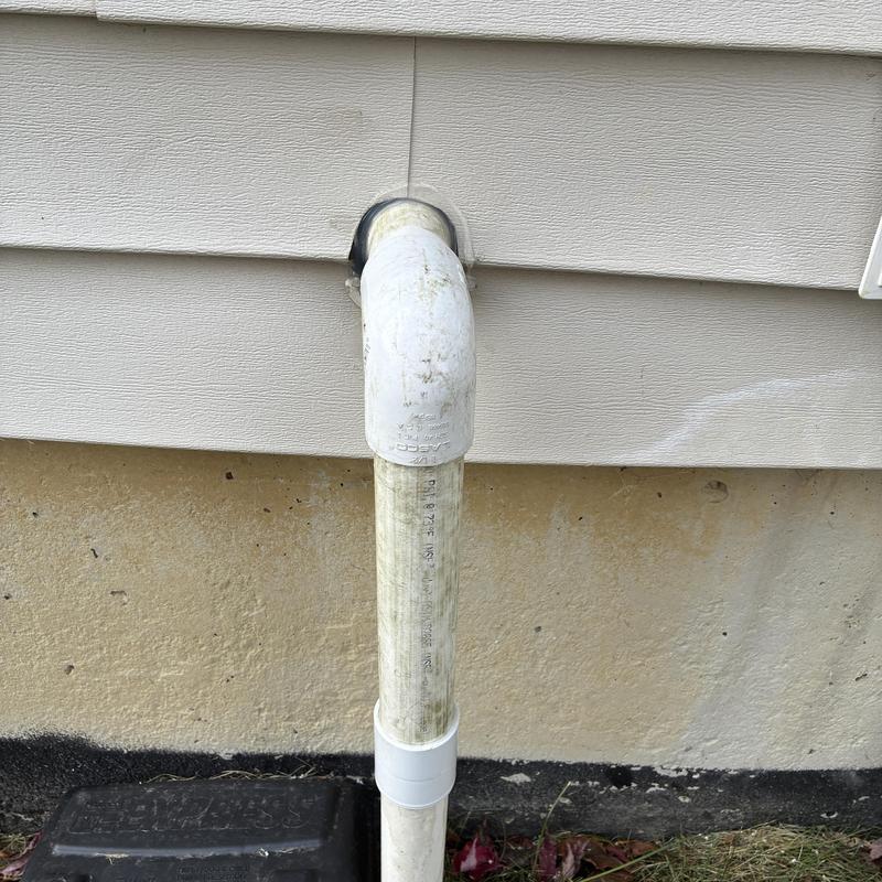 Sump pump discharge pipe attached to house exterior wall
