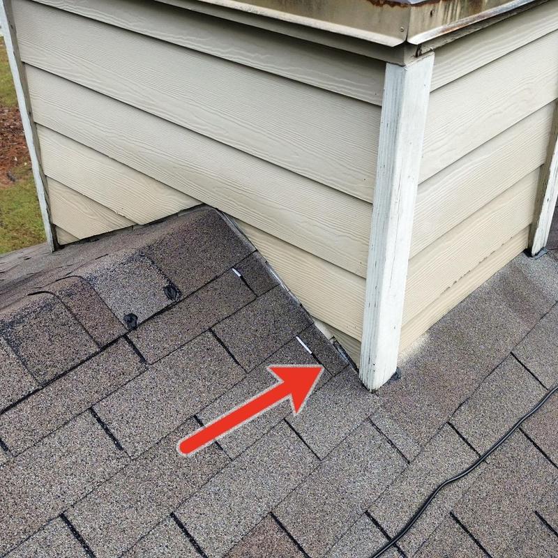 Damaged roof shingles near chimney base with arrow
