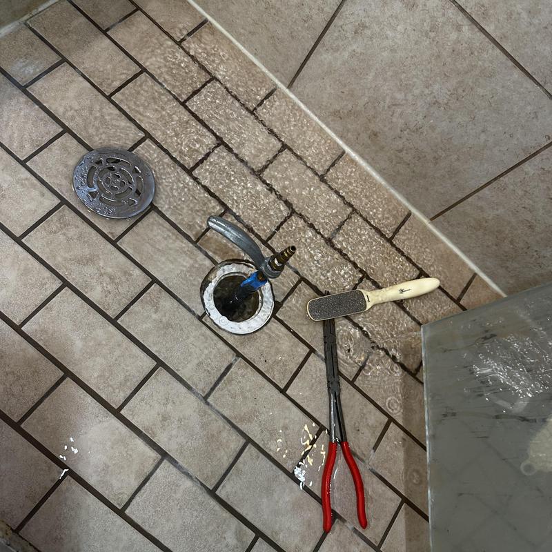 Shower drain pan leak test with tools on tiled floor