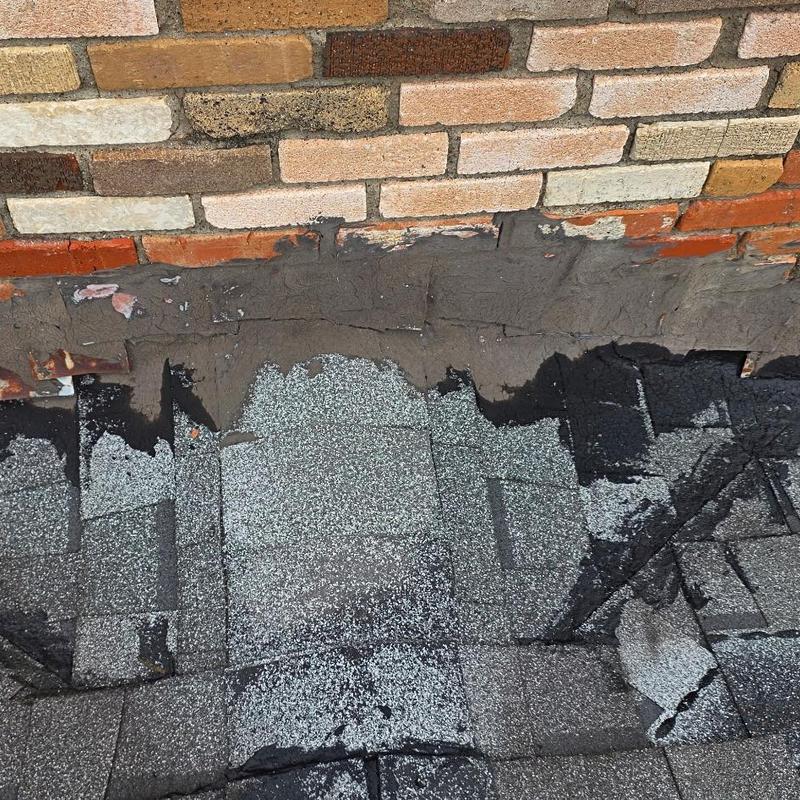 Roof shingles with damage near brick chimney base