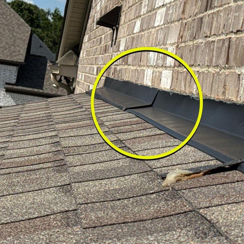 Roof flashing on shingled roof near brick wall