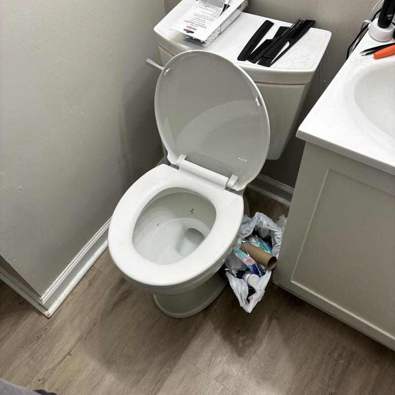 Toilet with open lid and trash can nearby