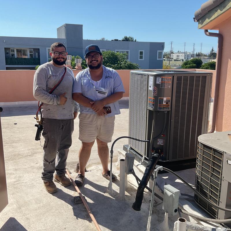 Heat pump installation on rooftop with two technicians