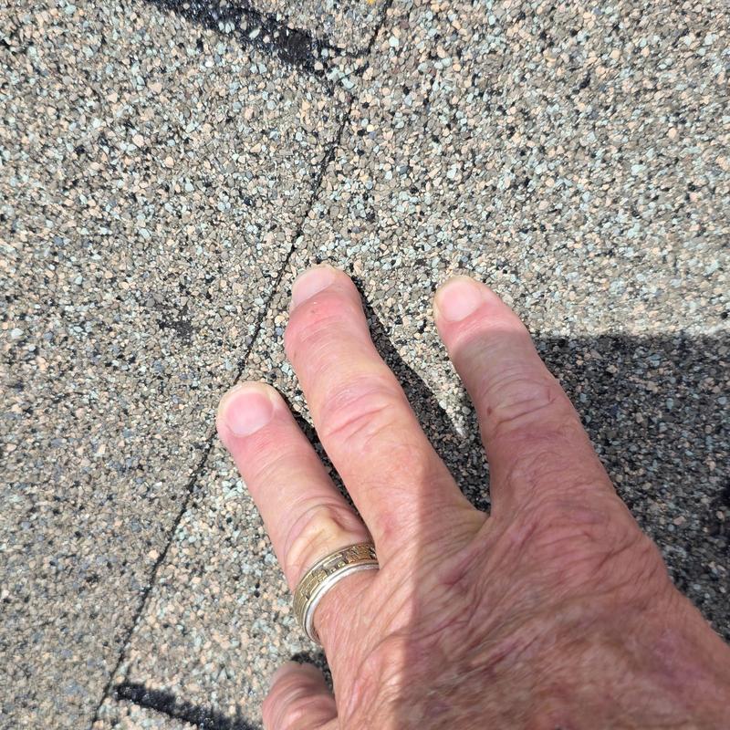 Asphalt shingle roof hail damage close-up with hand