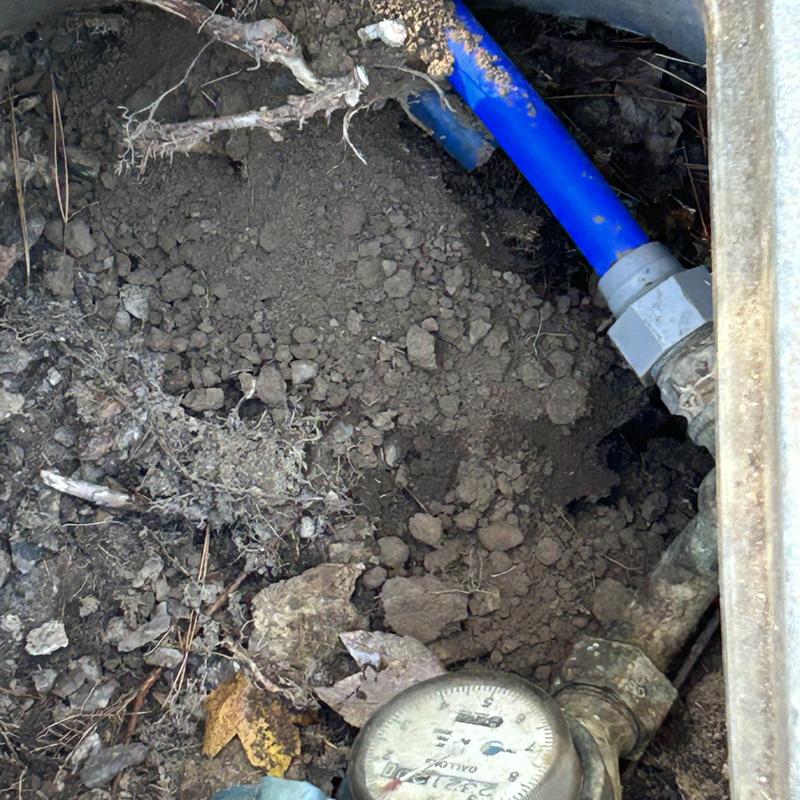 Water service pipe with meter and blue tubing exposed in soil