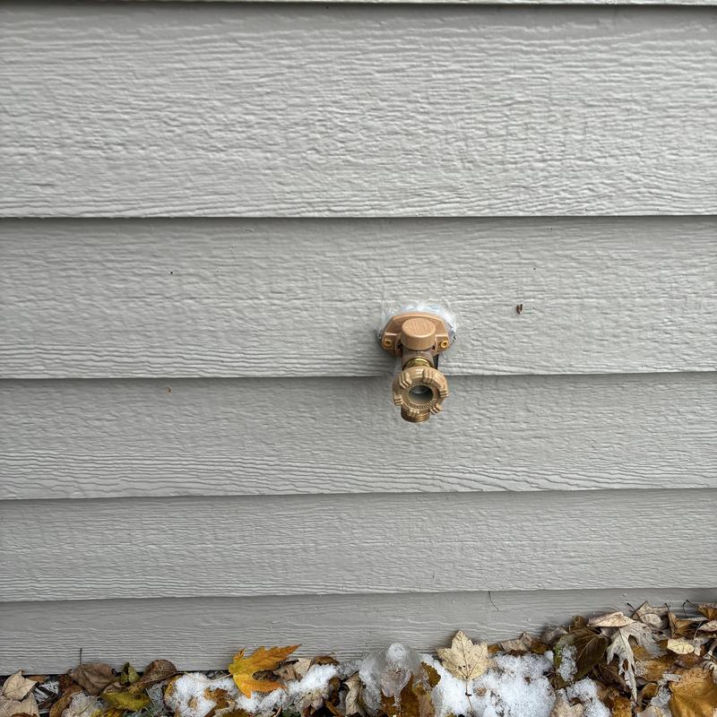 Outside hose faucet installed on gray siding wall