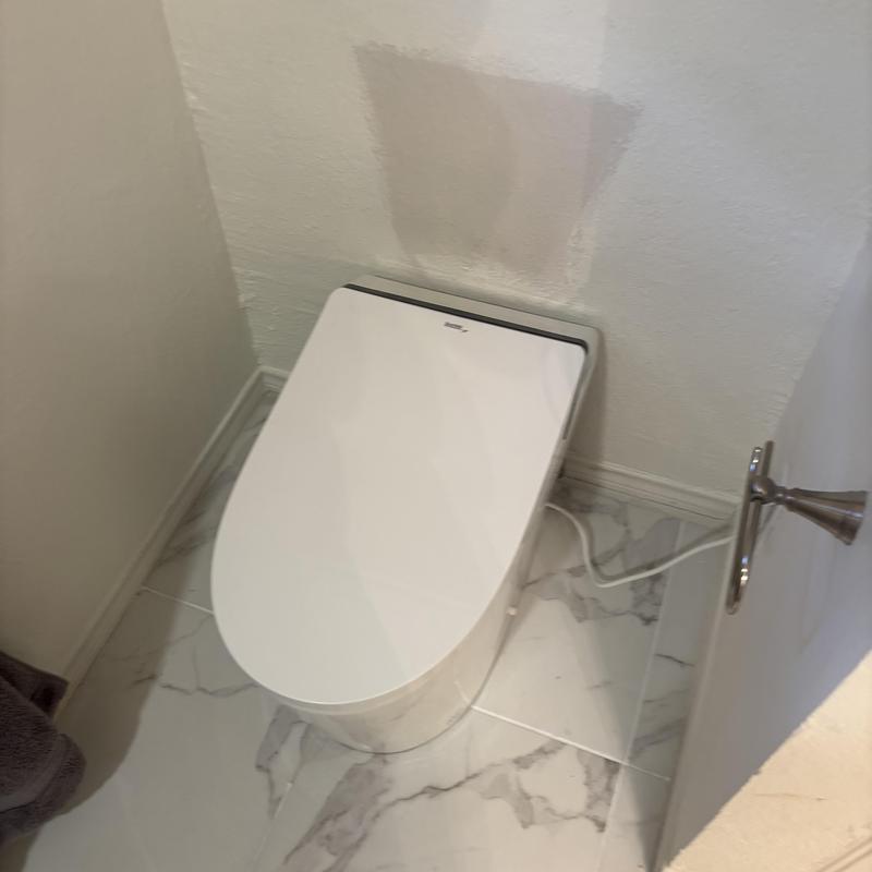 Toilet with integrated bidet installed in bathroom corner
