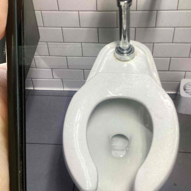 Toilet bowl with chrome flush valve and white tile wall