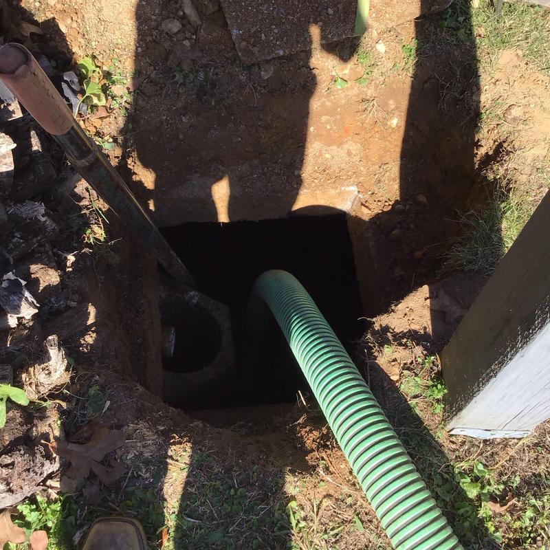 Septic tank with green pump hose and shovel nearby