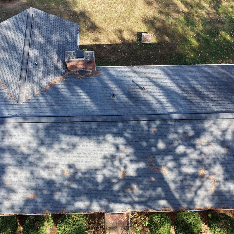 Asphalt shingle roof with chimney and vent pipes under shadows
