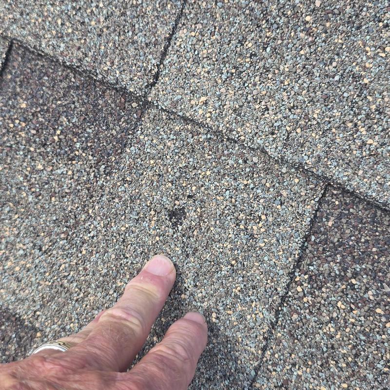 Roof shingles with hail damage spot pointed by hand Roof shingles with hail damage spot pointed by hand
