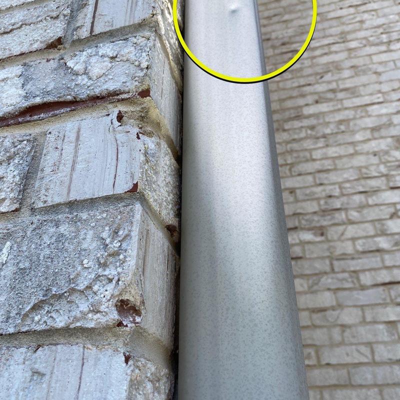 Metal downspout dent near brick wall corner