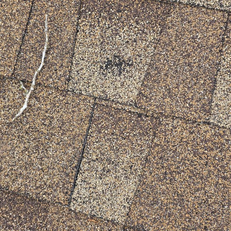 Asphalt roof shingles with dark water stain and debris.