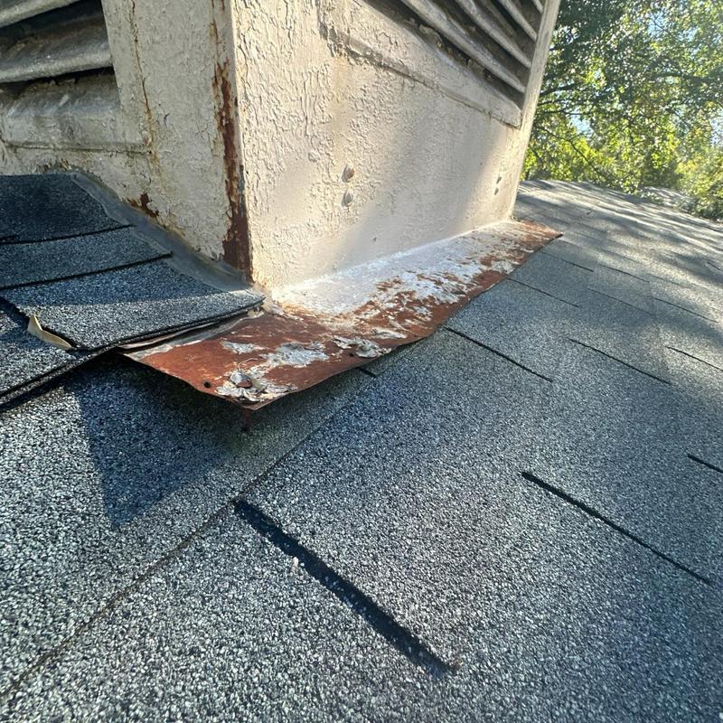 Chimney flashing with worn paint and rust on asphalt shingles