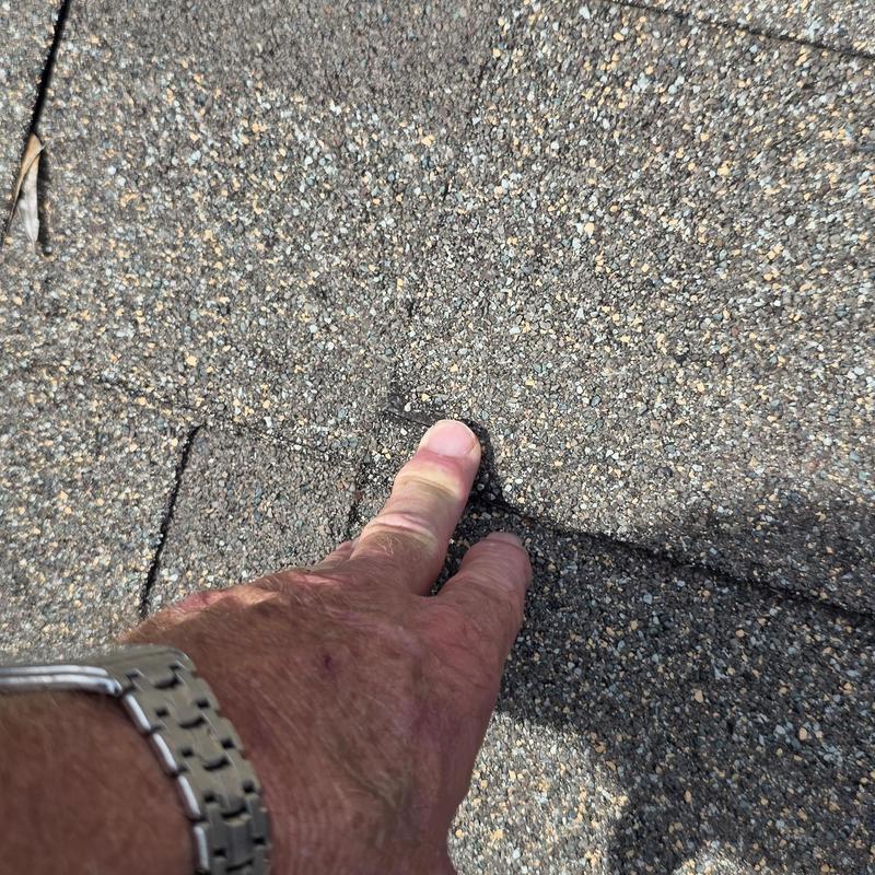 Asphalt roof shingle damage inspection close-up with hand