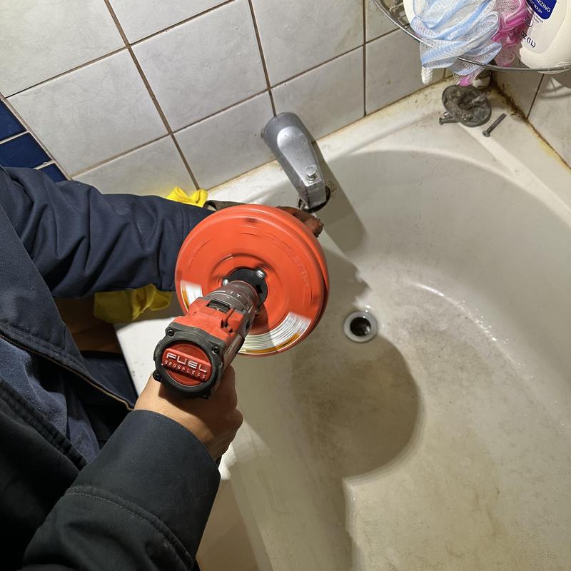 Tub drain clearing with plumber's snake tool in bathtub