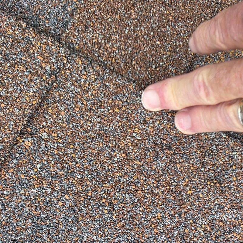 Asphalt roof shingle hail damage close-up with hand