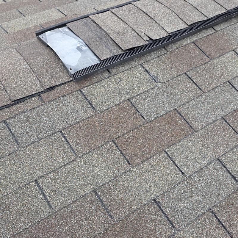 Roof shingles lifted near ridge vent on asphalt roof
