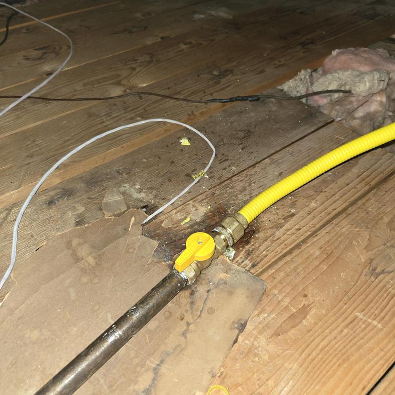 Copper gas line with yellow shutoff valve under floorboards
