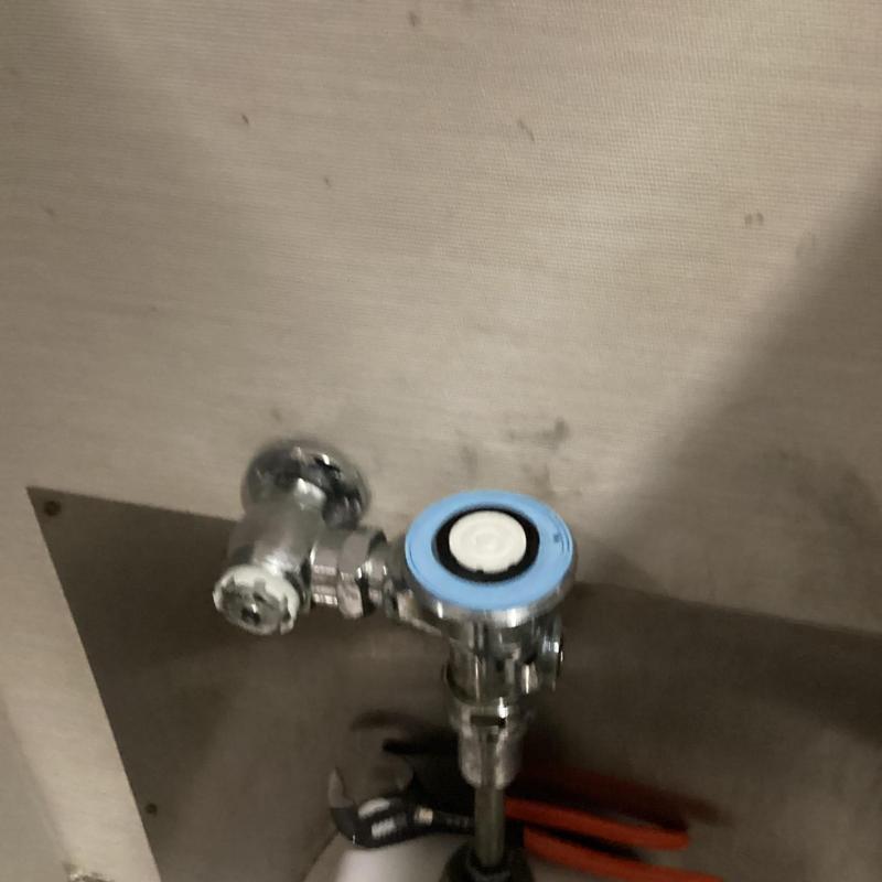 Flush valve assembly on urinal with plumbing tools nearby