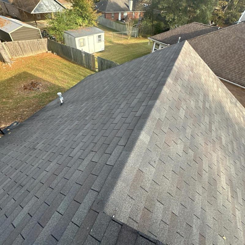Asphalt shingle roof ridge with vent pipe and backyard view