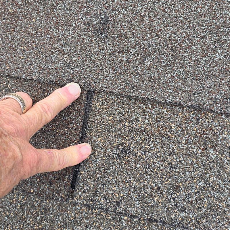 Asphalt roof shingle with gap being inspected for leaks