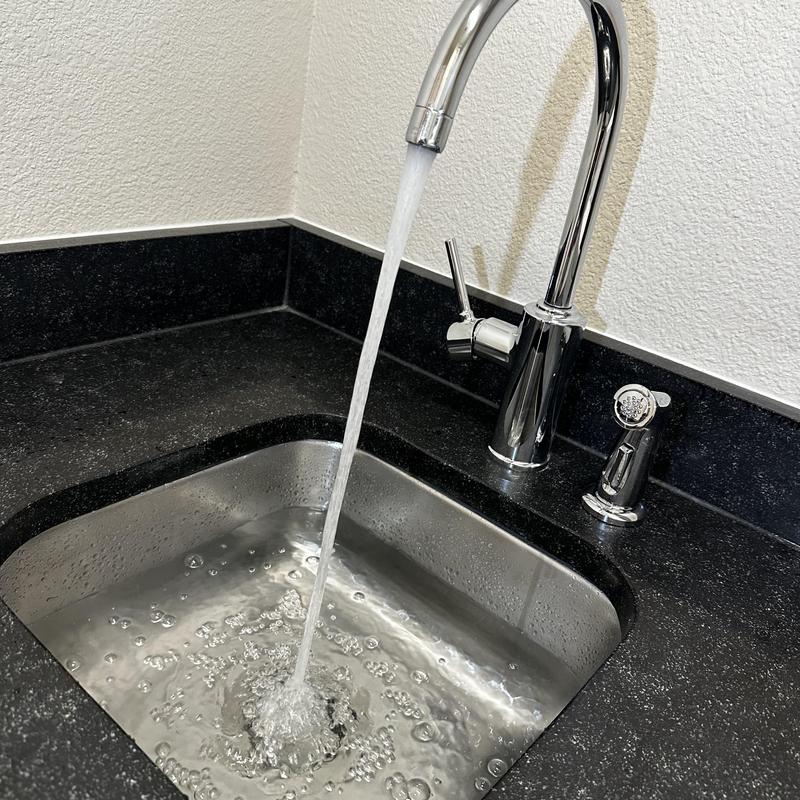 Kitchen faucet with sprayer flowing water in black countertop