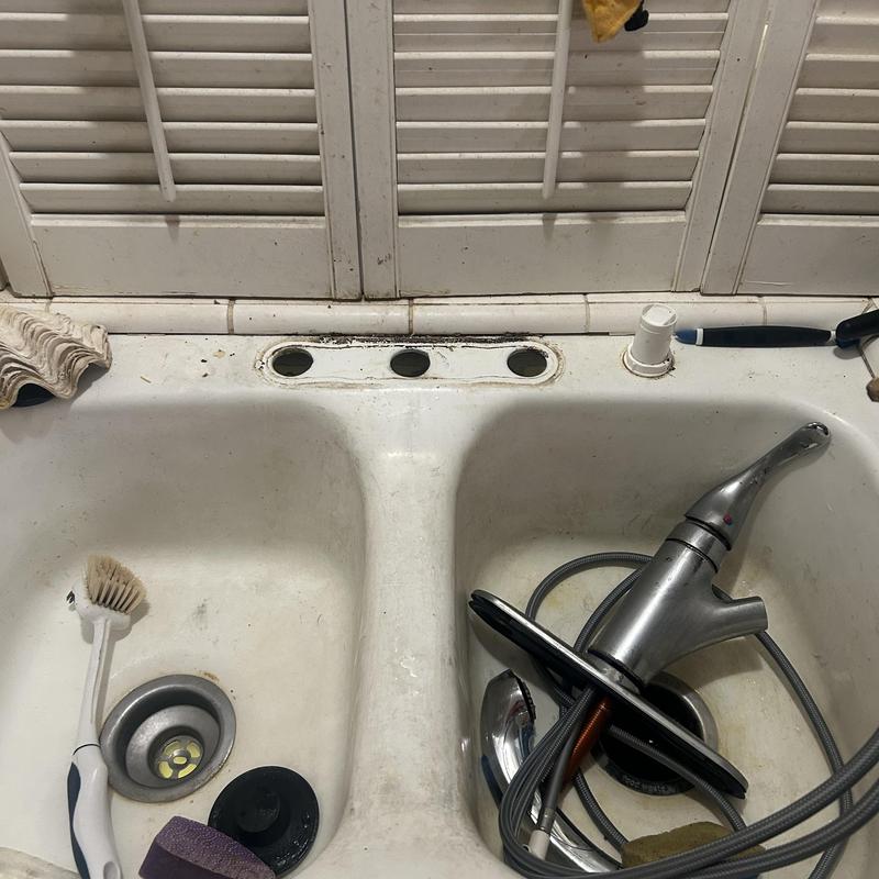 Kitchen sink faucet removed with old parts inside sink basin