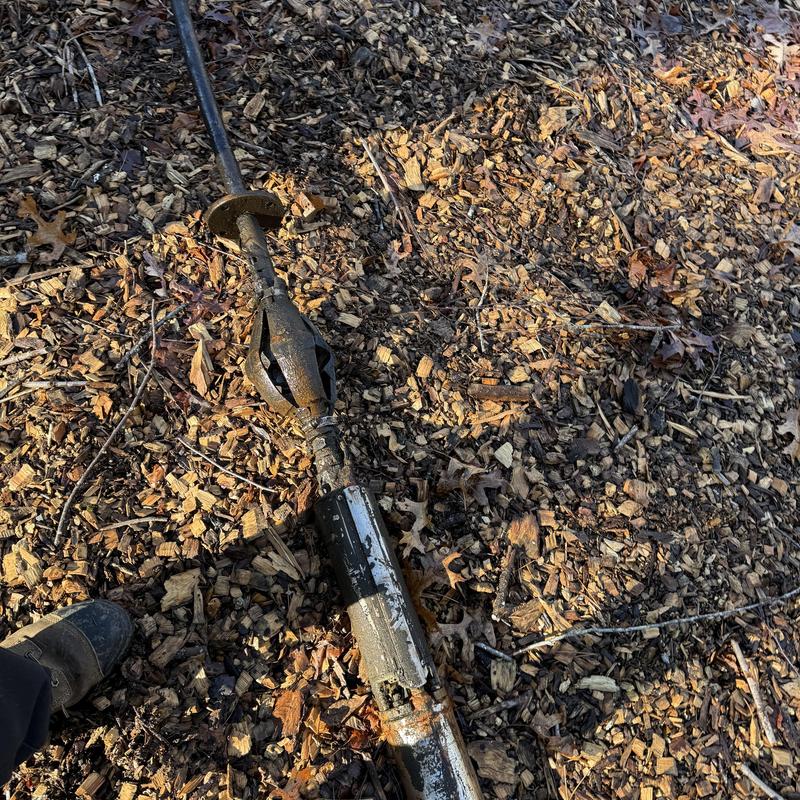 Well pump removed and resting on wood chips outdoors