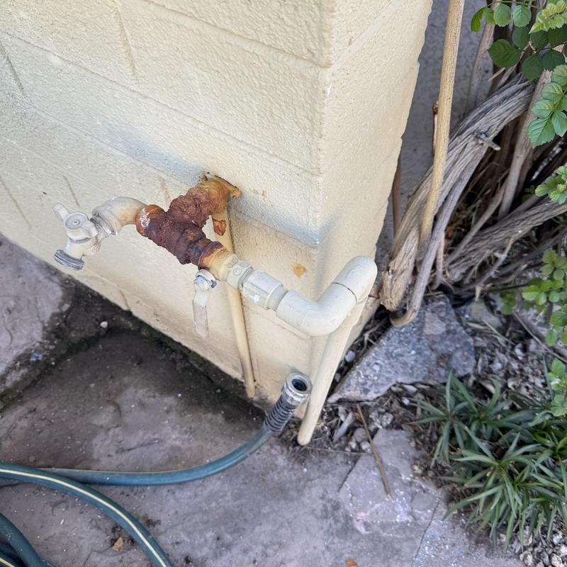 Rusty hose bib with piping on exterior wall