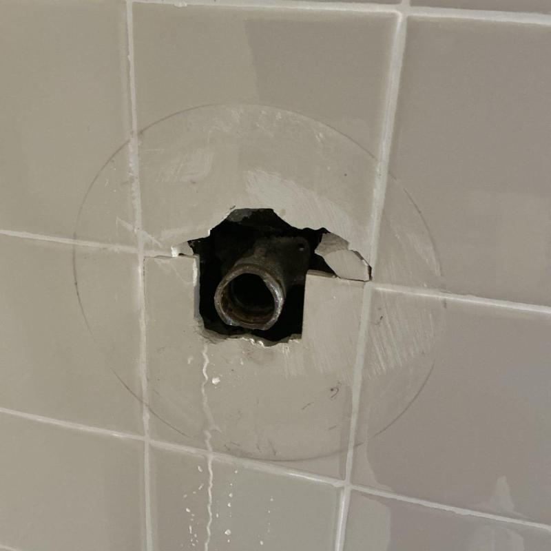 Shower valve pipe exposed in tiled bathroom wall