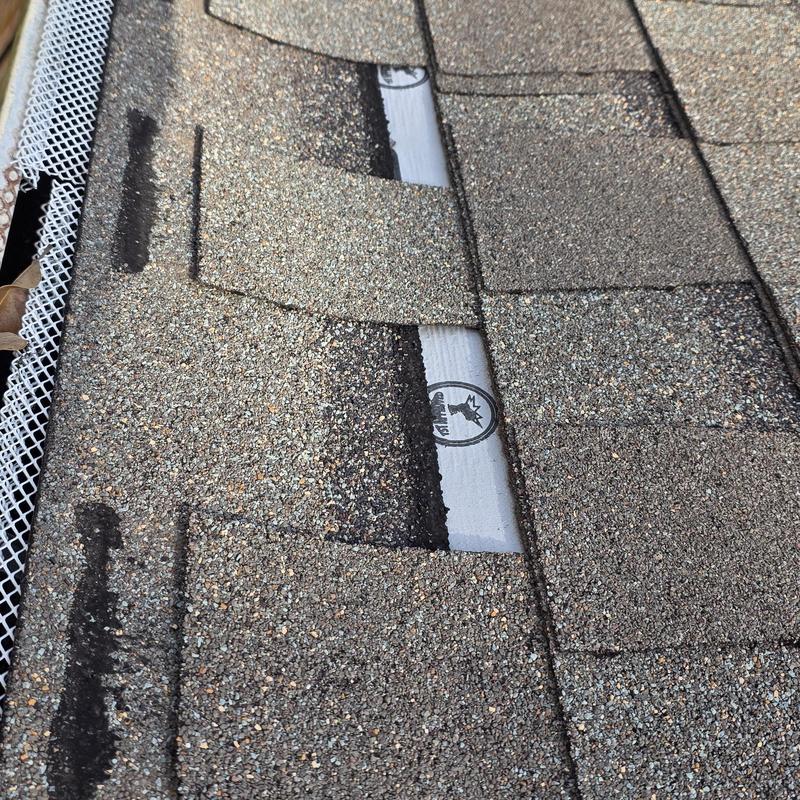 Asphalt roof shingles with storm damage and exposed underlayment