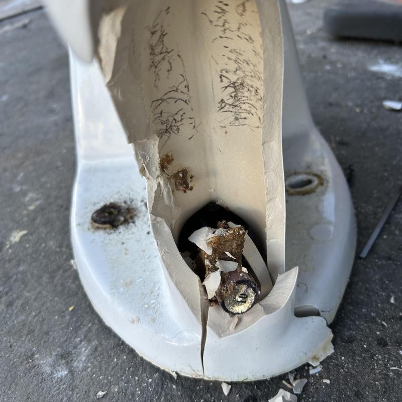 Toilet base cracked with rusted bolt and debris inside